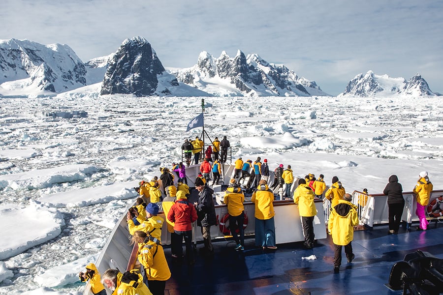 Passengers stand at the hull of the ship as they cruise through sea ice