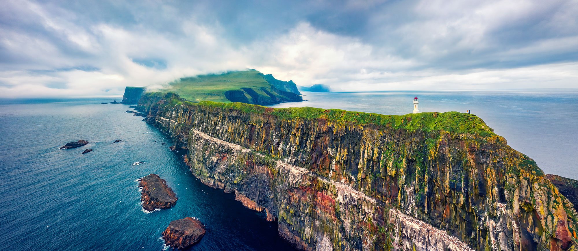 Grassy Cliff of the Faroe Islands with a Lighthouse in the distance.