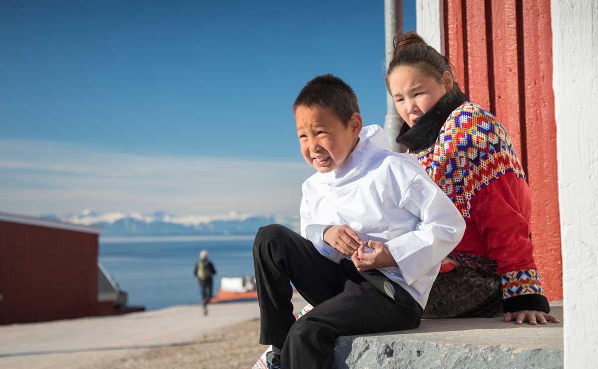 Children sitting on a stoop in an arctic community enjoy the sun.