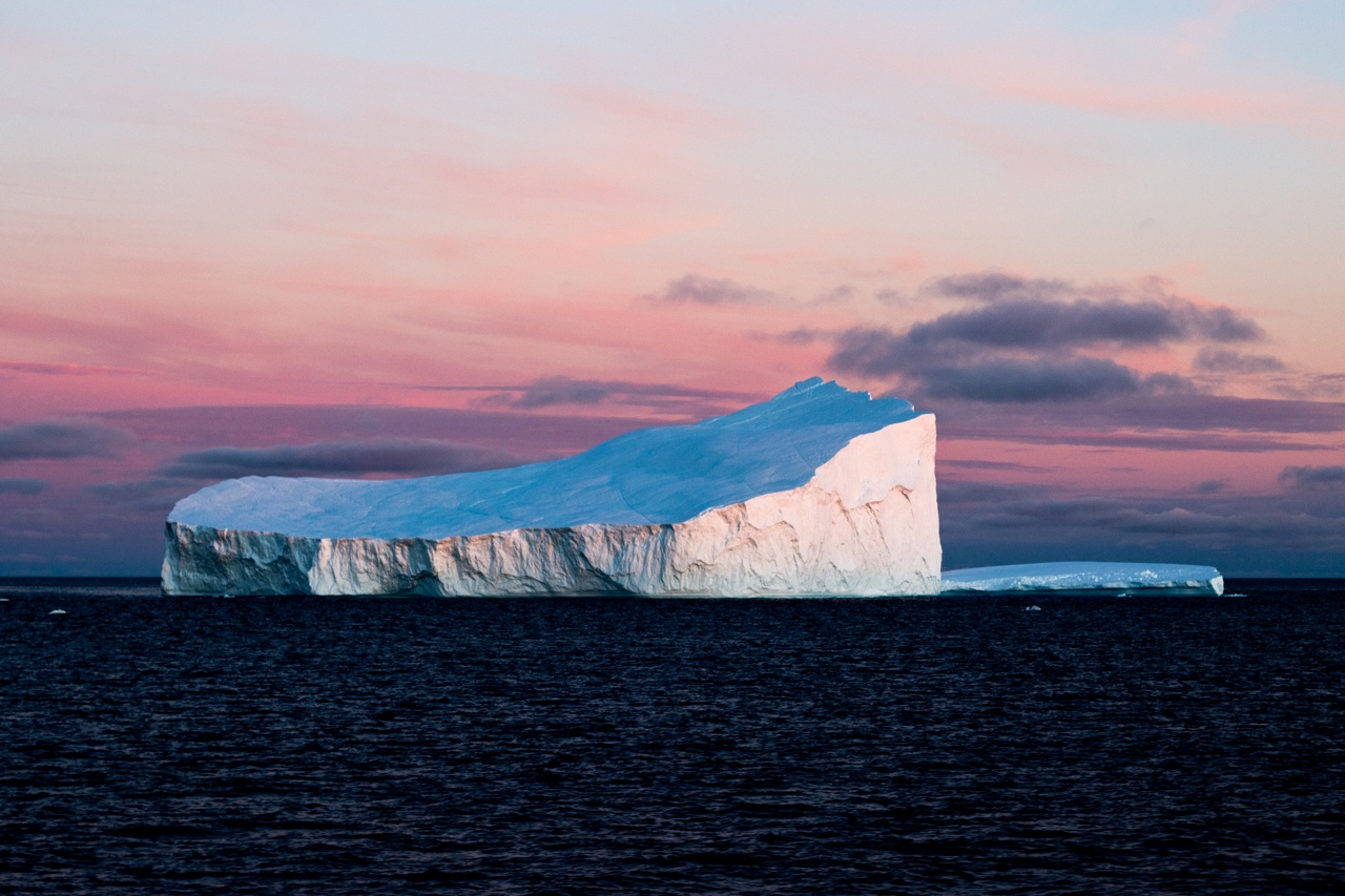 An imposing iceberg in stark contrast to the warm-colored Arctic sky.