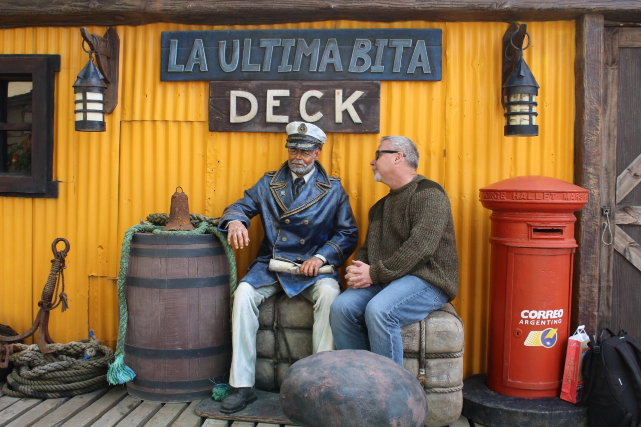 Quark passenger Richard Thomas, on Day One of his Antarctic Explorer: Discovering the 7th Continent expedition, visits the backyard of La Ultima Bita and poses with a life-sized ship’s captain figurine on a self-guided tour of downtown Ushuaia. 