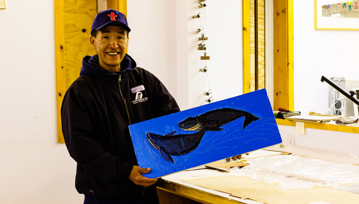 A man holds a painting of two whales.