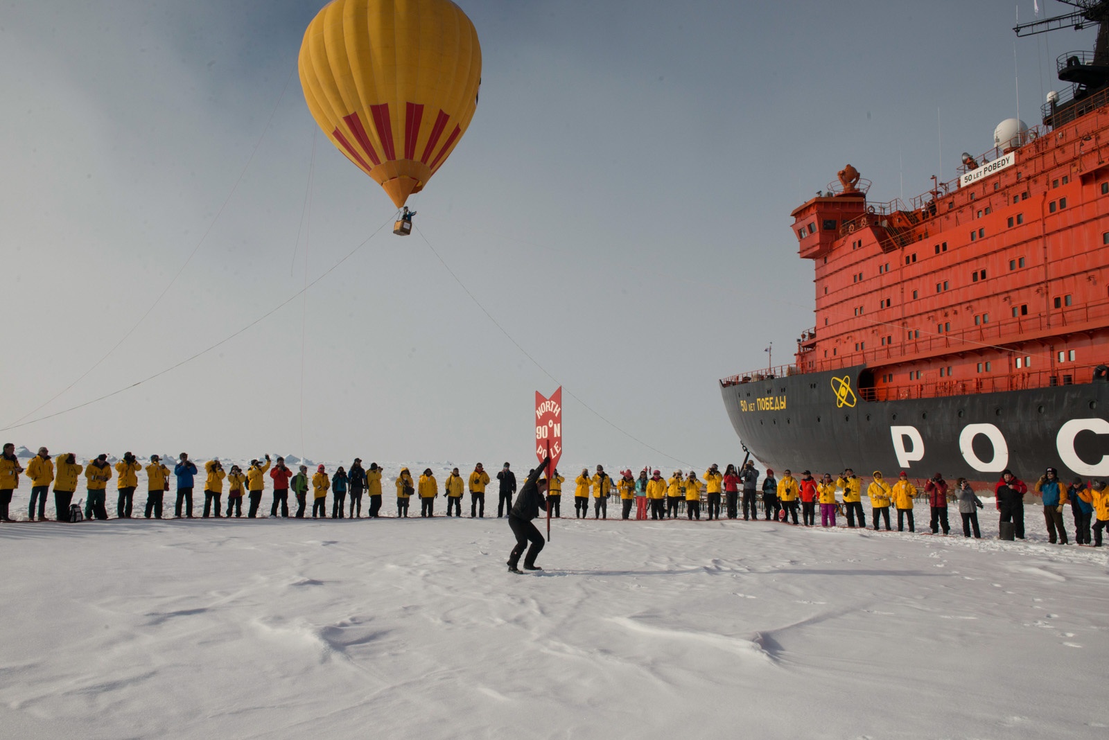A hot air balloon flies high overhead as North Pole expedition passengers celebrate reaching their destination.