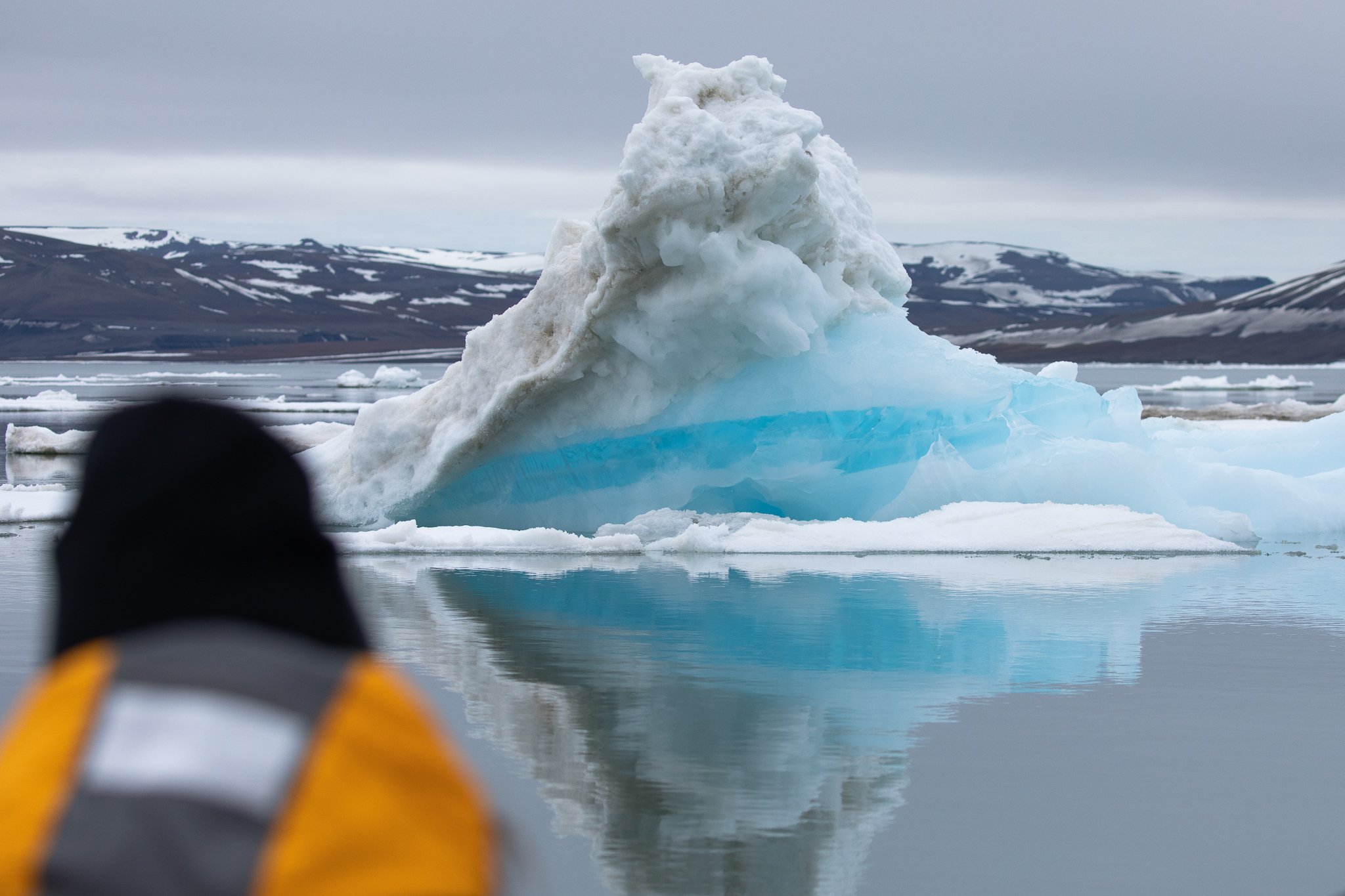 A Quark Expeditions guest is mesmerized at the sight of a blue iceberg in Svalbard, in the heart of Arctic Norway.