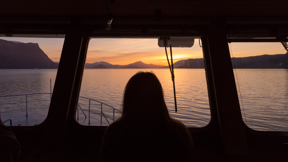 Silhouette of a woman looking across the bow of the ship towards a sunset horizon.