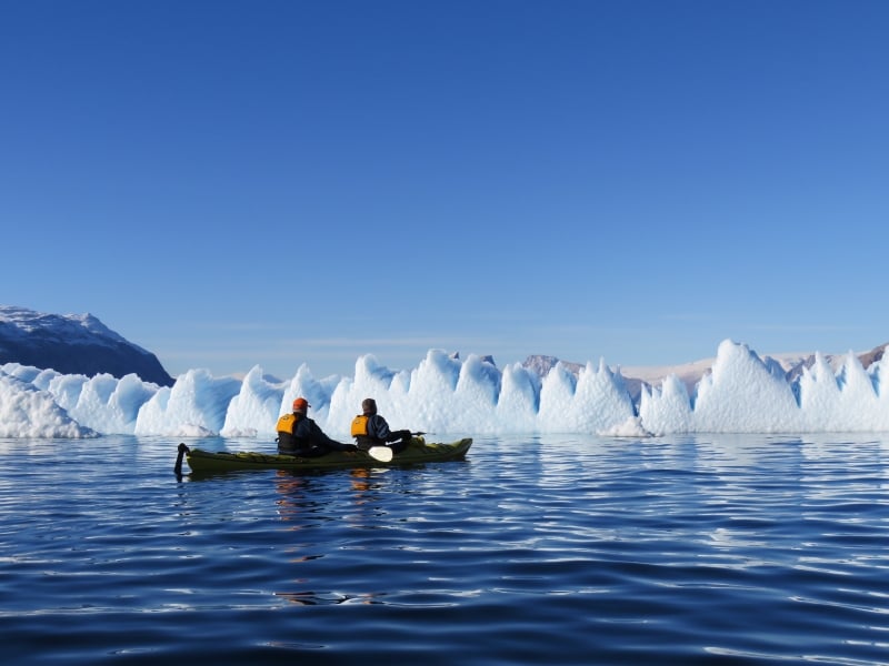 Kayakers take a moment to appreciate a massive wall of ice in their path while on Arctic expedition.