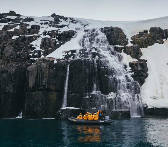 Zodiac cruising near waterfall in the Arctic